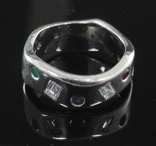 A modernist wavy design 18ct white gold, emerald, ruby, sapphire and baguette cut diamond gypsy set ring, size R.
